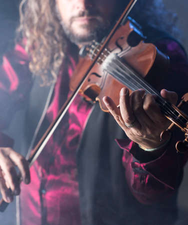 handsome man playing classical violin through blue smokeの写真素材