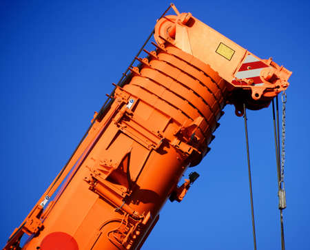 Zoom shot of an orange-coloured truck-mounted crane with telescopic boom pushed together, blue skyの写真素材