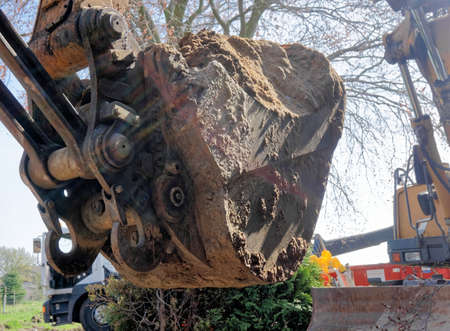 Large excavator shovel filled with a mighty load of loose brown sand at the construction site,...