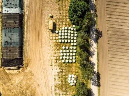Aerial view of a farm warehouse, vertical photographed round silage bales wrapped in foils, made with droneの写真素材