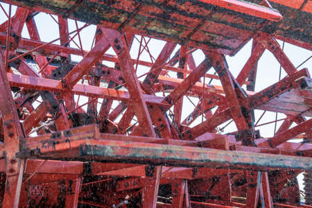 Detail view of a rotating red paddle wheel of a paddle wheel steamer, with water splashes and slight...