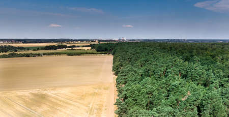 Abstract image of a harvested wheat field, divided at a forest boundary, in the middle, with blue...