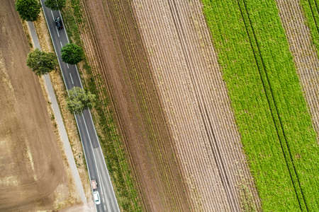 Abstract vertical aerial view of a narrow country road at the edge of an area of arable land with...