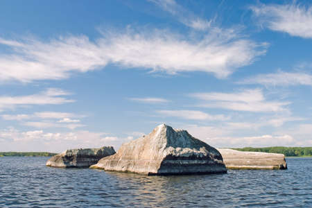 Rock on the water under cloudy skyの写真素材