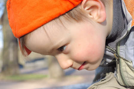 Little boy in orange sideward turned cap looking downの写真素材