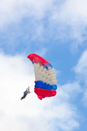 Man with three-colored parachute against cloudy skyの写真素材