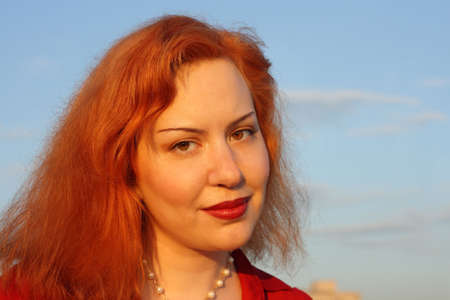 Face of red-haired woman against blue sky lit by setting sun