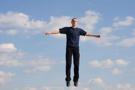 Jumping teenage boy in dark blue t-shirt against cloudy skyの写真素材