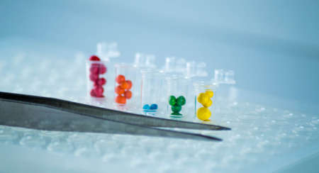 Close-up of tweezers and test tubes with multicolored liquid.