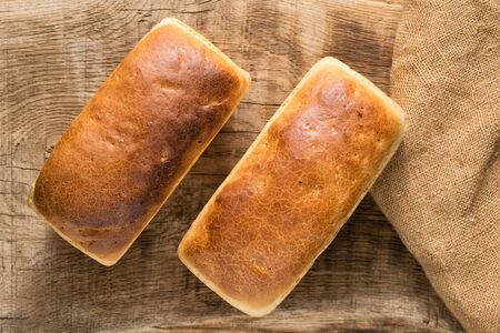 Two loaves of white bread on an oak board