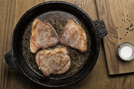 three fried pork steaks on a frying pan on a wooden tableの写真素材