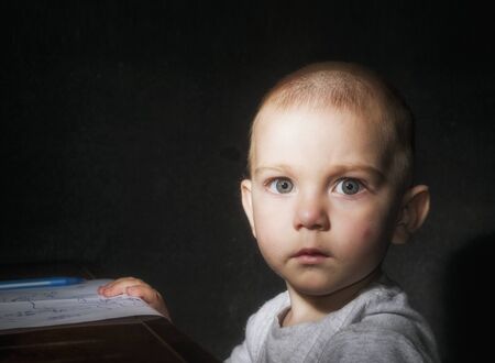 Blond blue-eyed child with a surprised look and a dirty mouth after eating on a black background