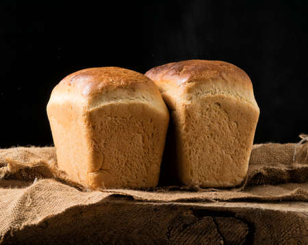 Two loaves of white bread on an oak board