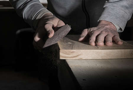 Detail of male hand using a sanding block to sand timber deskの写真素材