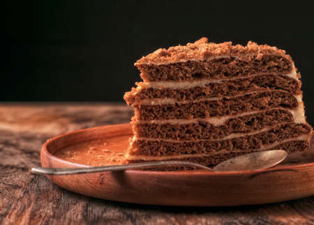 A piece of homemade honey cake, on a wooden plate and an old teaspoon. On an oak table On a black...