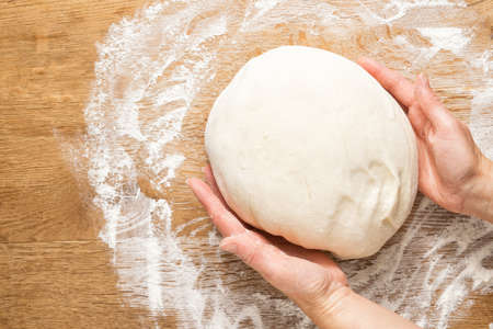 Female hands knead pizza dough on a wooden table still lifeの写真素材