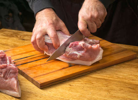 The cook cuts a large knife pork ham on a cutting board.