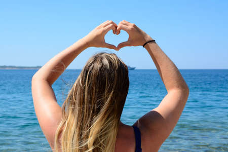 Girl shows heart from his hands by the seaの写真素材