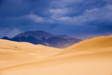 Thunder clouds, rain and sand are being blown over great sanddunes 