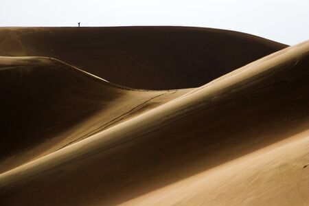 People small like aints walking far-away in dunes with sand being blown over by windの写真素材