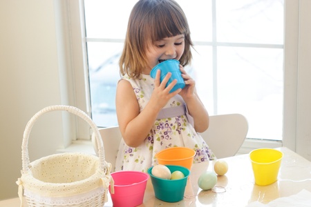 Small girl playing and painting Easter eggs in a room with a lot of sun light