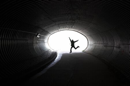 Jumping girl silhouette inside dark long tunnel の写真素材