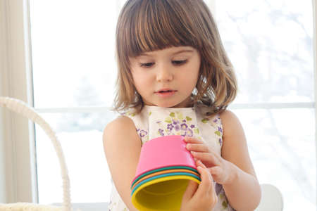 Small girl playing with colorful buckets in a room with a lot of sun light