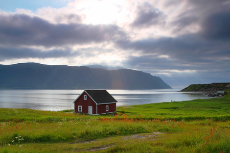 Red wooden cabin on the shore in Nordic landscapeの写真素材