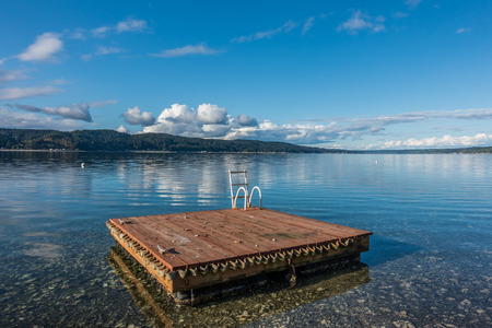 A wooden swim float sits on Hood Canal in Washington State. Blue cloudy skies are reflected in calm waters.の写真素材