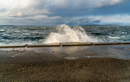 A vave explodes onto the sea wall at Alki Beach in West Seattle, Washington.の写真素材