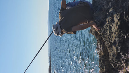 A man climbs a rock in the sea against the background of a blue skyの写真素材