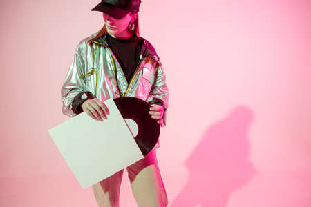 The girl with the vinyl record. Colored background and neon light. Modern clothes. Music poster....