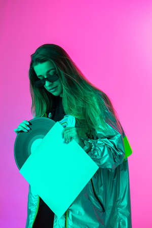 The girl with the vinyl record. Colored background and neon light. Modern clothes. Music poster. Retro concept.の写真素材
