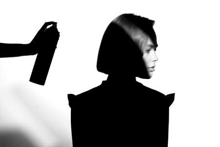 Black and white silhouette portrait with shadow and spot of light. The girl uses hairspray. Hair cosmetic concept.の写真素材