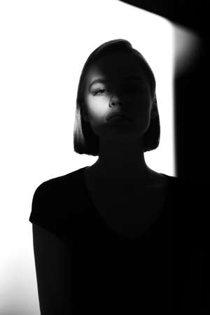 Fashionable beauty portrait. Black silhouette on white background. Girl with a spot of light on her face.の写真素材