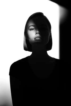 Fashionable beauty portrait. Black silhouette on white background. Girl with a spot of light on her face.の写真素材
