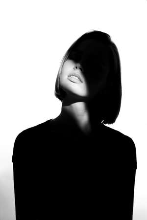 Fashionable beauty portrait. Black silhouette on white background. Girl with a spot of light on her face.の写真素材