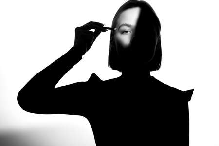Portrait of a girl on a white background. Fashion model uses cosmetic pencil for eyebrows and eyelids. Black-white.の写真素材
