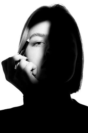Portrait of a girl on a white background. Fashion model uses cosmetic pencil for eyebrows and eyelids. Black-white.の写真素材