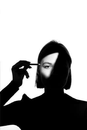 Portrait of a girl on a white background. Fashion model uses cosmetic pencil for eyebrows and eyelids. Black-white.の写真素材