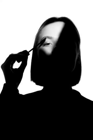 Epic promotional portrait of a girl with applicator and mascara brush. Black and white minimalistic advertising concept.の写真素材