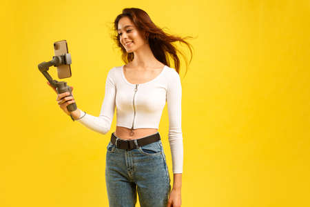 Young blogger girl with three-axis electronic stabilizer gimbal. Makes a selfie and video blog.の写真素材