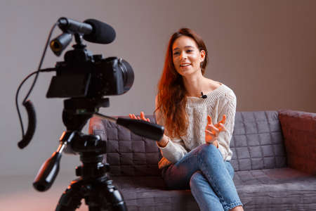 Young teen girl vlogger makes a video stream on the couch at home. A video camera on a tripod.の写真素材