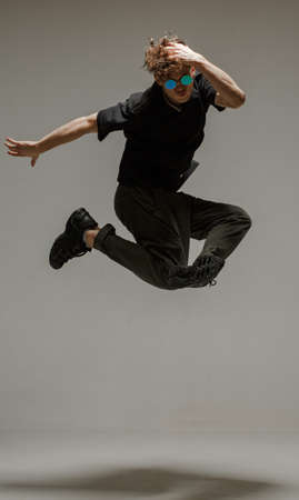 Guy dancing contemporary dance in studio. Neutral grey background. Acrobatic bboy dancer.
