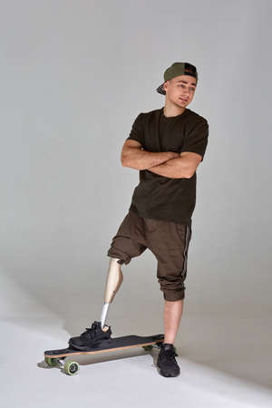 Disabled young man with leg prosthesis with longboard skateboard on white background. Sun light.