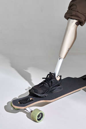 Disabled young man with leg prosthesis with longboard skateboard on white background. Sun light.の写真素材
