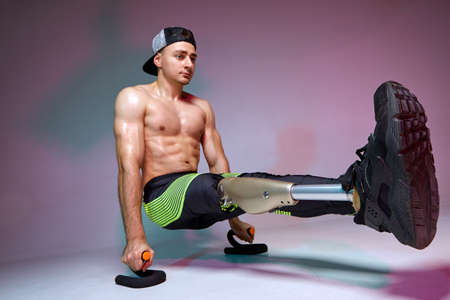 A young muscular man with a disability with a prosthetic leg is training in a gym. Motivation workout poster.の写真素材