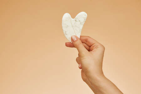 Beautiful girl hand with beauty gua sha quartz stone for massage. Beige background isolated. Cosmetic natural trend.の写真素材
