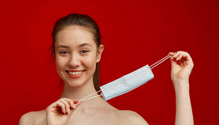 A happy young girl with a medical mask on a red background. Poster about the coronavirus COVID-19...
