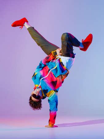 Guy dancing contemporary dance in studio. Neon light grey background. Acrobatic bboy dancer. Break...